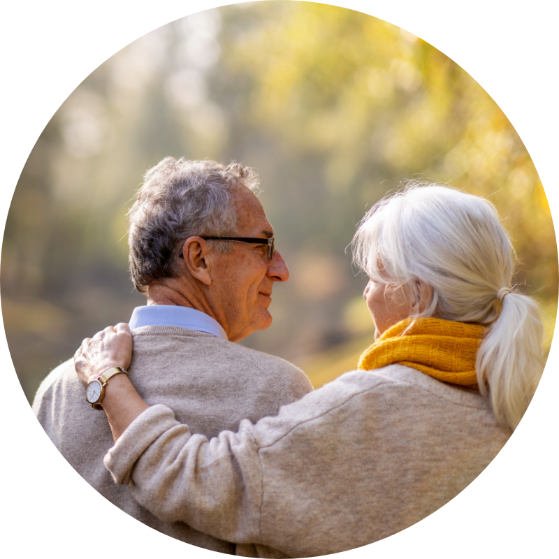 an older adult couple looking at each while the woman puts her arm around the man's shoulder