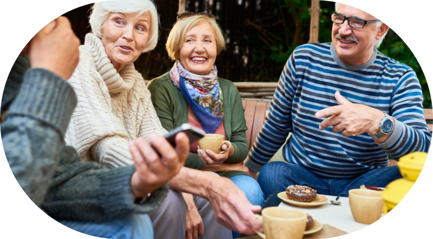 a group of four senior adults sit outside talking to each other and laughing