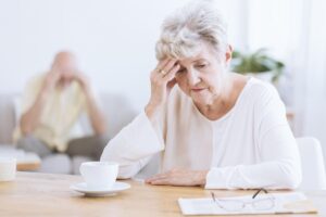 a senior woman sits at a table with her hand to her head wondering if she needs dementia patient care