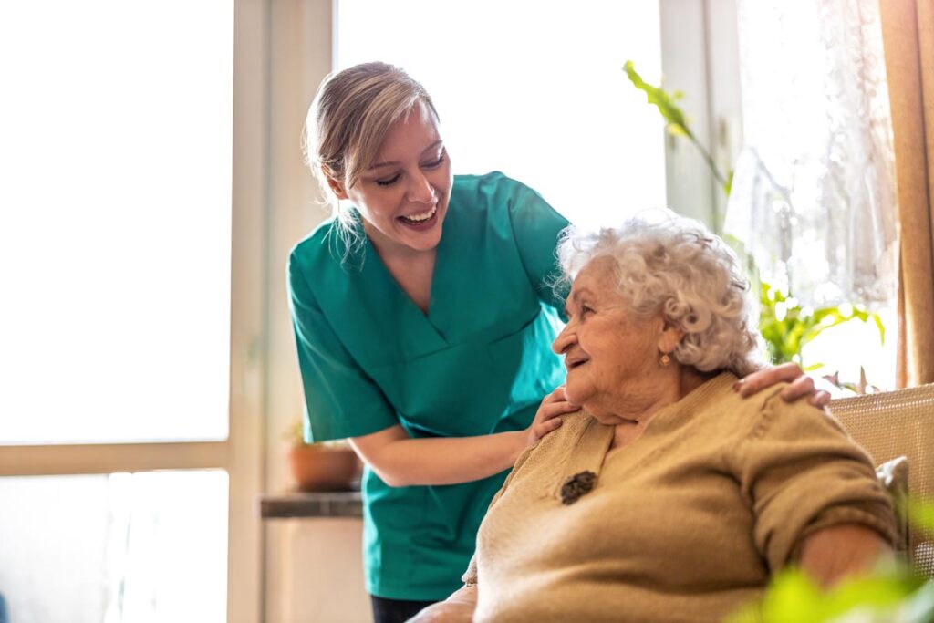 nurse smiles and helps a senior woman while she sits and endures the benefits of palliative care