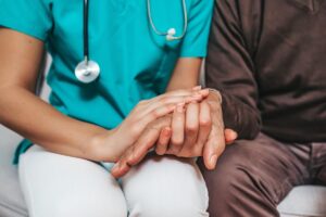 nurse holds the hand of a senior while explaining what is involved with palliative care services